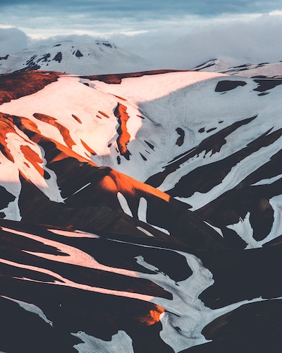 snow-covered icelandic mountains touching clouds and orange sunset