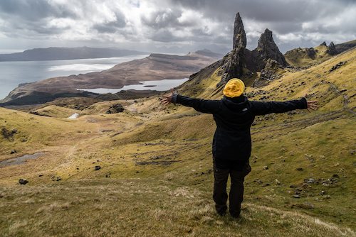 A woman with her hands in the air facing the national park on the Isle of Skye