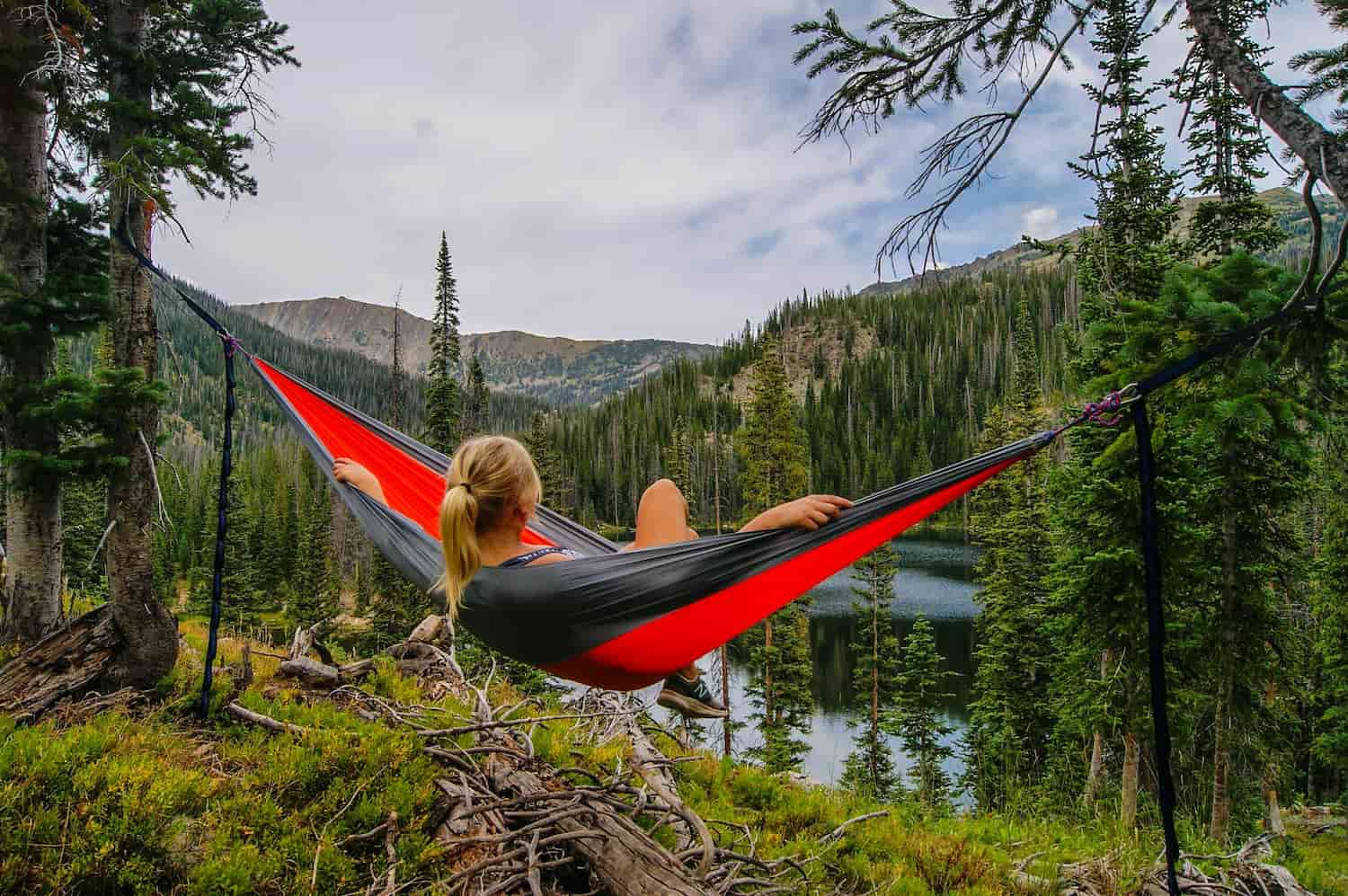 A girl is laying in a hammock, looking out into the forest and mountains