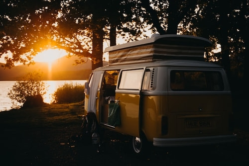 A VW campervan parked next to a lake with the sunset in the background.