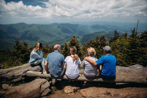 A family of 5 sat on a tree log looking out into the mountains.