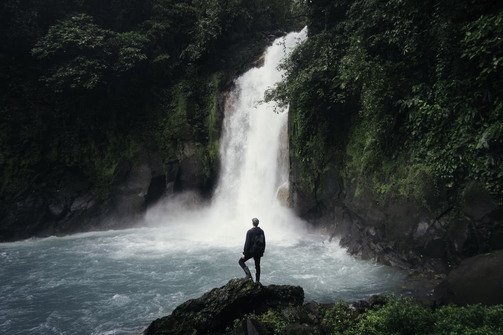 A man standing on a rock in front of a waterfall