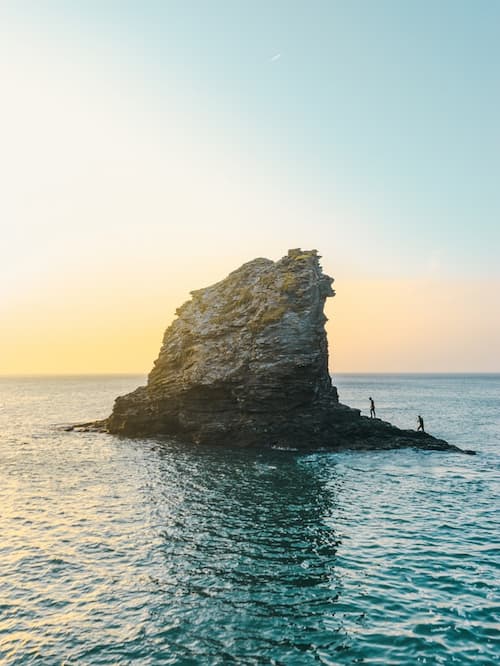 Two people climbing a rock in Trevellas Cove in Saint Agnes overlooking a sunset