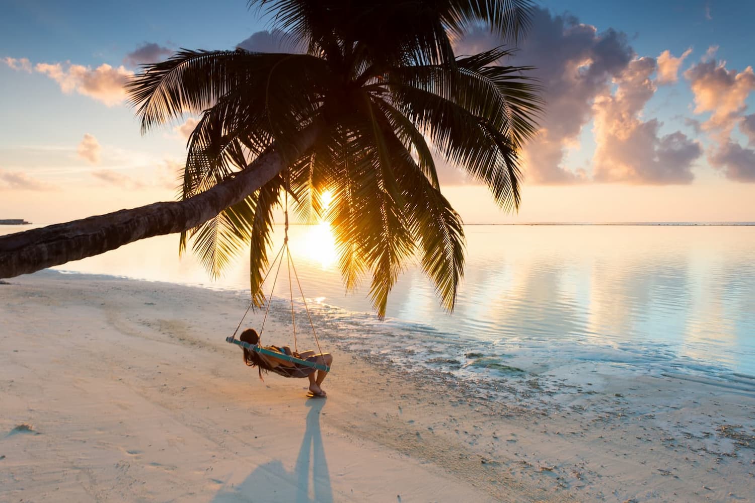 Woman relaxing in a hammock swing on beach overlooking blue water