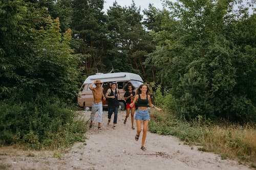 Friends on a California roadtrip running from Volkswagen van to sandy beach