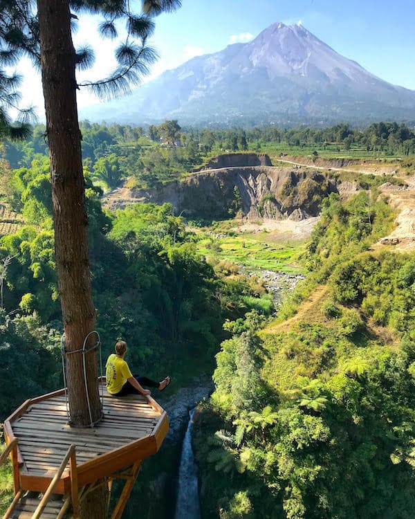 DAYMADE winner, Sam, sits on a treetop walkway overlooking a large mountain in the distance