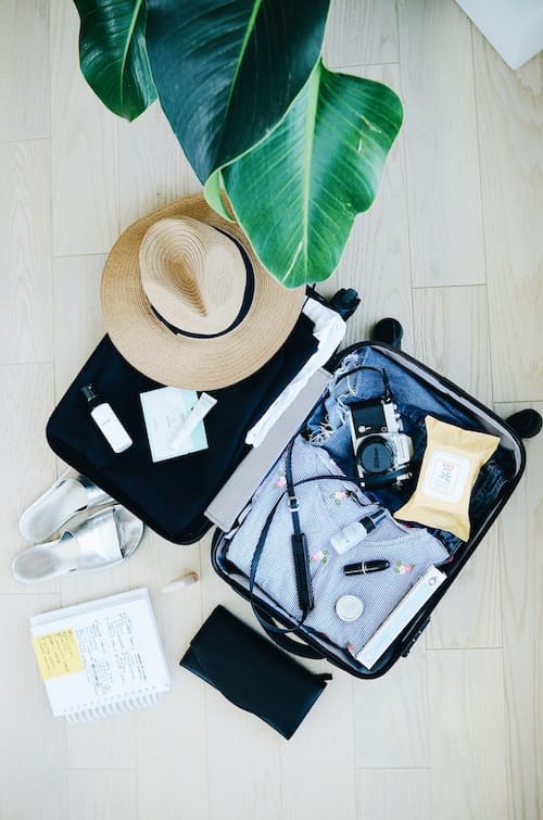 A suitcase opened with holiday clothes, a sun hat, a camera, and toiletries.