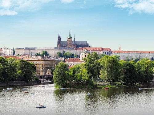 A city landscape view of Prague, boats on the river, and the cathedral.