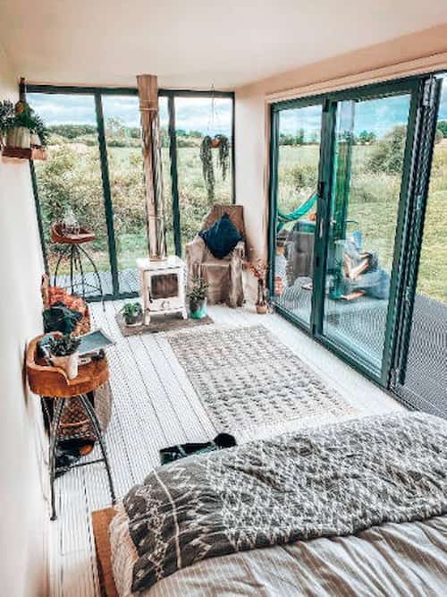 A bright bedroom with a fireplace and glass doors surrounded by nature.