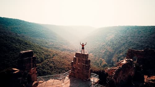 man standing on top of mountain overlooking a valley with his hands up in the air