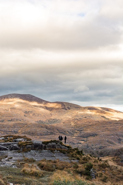 three people hiking across mountainous region in Wales with clouds casting patterns on the grassy hills