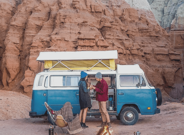 couple stood outside VW camper-van by a wood fire